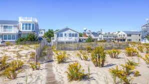 A beachfront property with a wooden walkway leading to a house with a balcony. - Beach Front! (Long Beach)