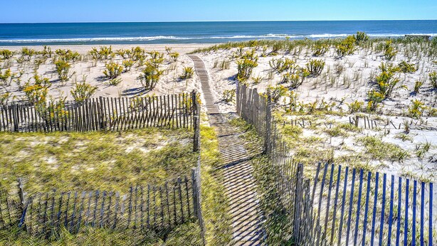 A sandy beach with a wooden pathway leading to the ocean. - Beach Front! (Long Beach)