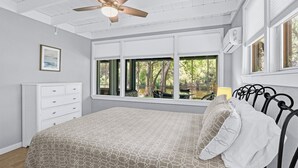 Un dormitorio con cama, ventilador de techo, cómoda y ventanas grandes.