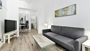 A modern living room with a flat-screen TV, grey sofa, glass coffee table, and a painting on the wall. - Modern Beachfront Suite 202 (Ocean City)