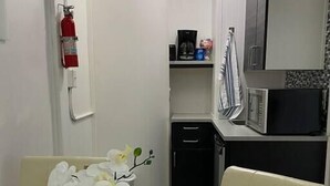 A small, modern kitchen with a microwave, a coffee maker, and a small refrigerator. There is a white table with a potted orchid in the center of the room. - Modern Beachfront Suite 202 (Ocean City)