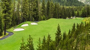 A golf course with sand bunkers, surrounded by dense forest and hills.