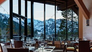 A restaurant with tables set for dining, large windows offering a mountain view, and a wooden ceiling structure.
