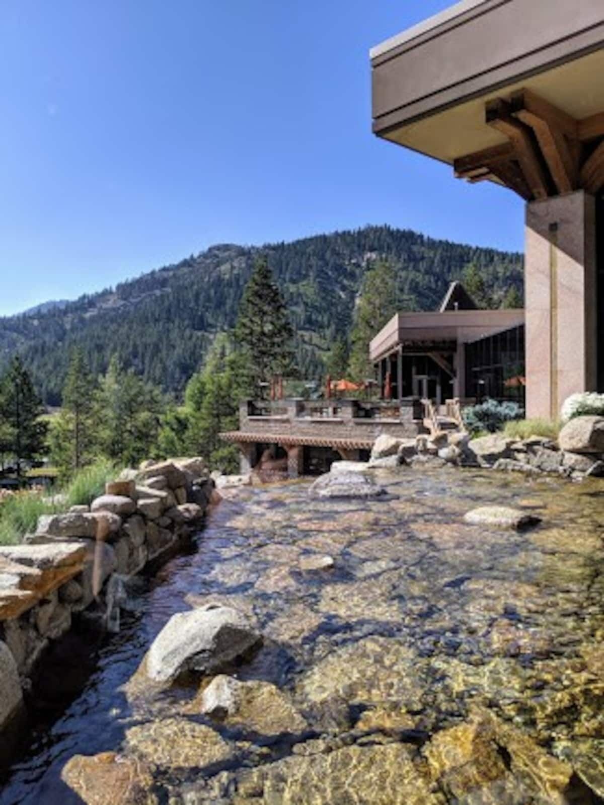 A building with a stone pathway leading to a wooden deck overlooking a clear stream.