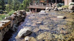 A building with a stone pathway leading to a wooden deck overlooking a clear stream.