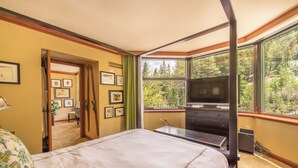 A bedroom with a bed, a television, and a large window offering a forest view.