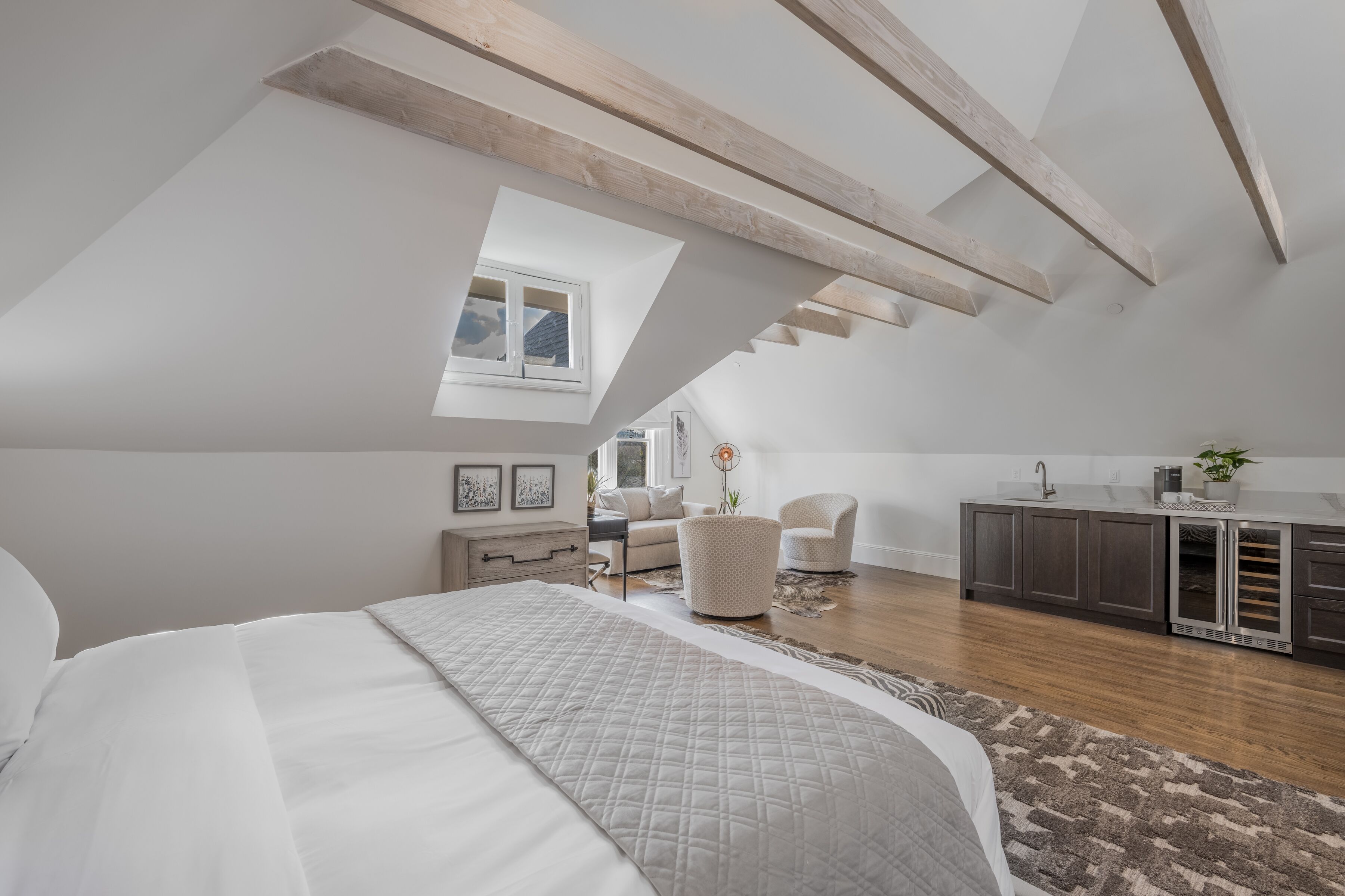 A modern loft bedroom with a skylight, a large bed, a kitchenette, and a seating area.