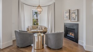 A living room with a sofa, two armchairs, a round coffee table, a fireplace, and a chandelier. - The George Luxury Boutique Inn (Napa)