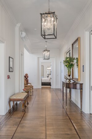 A hallway with a chandelier, a mirror, a console table with a vase, and a bench. - The George Luxury Boutique Inn (Napa)