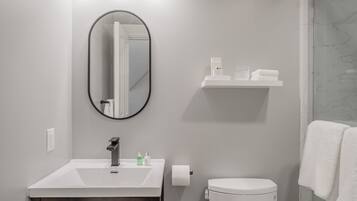 A bathroom with a white sink, mirror, and toilet. There is a shelf above the sink with toiletries.