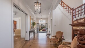 A spacious hallway with hardwood flooring, a chandelier, and a wooden staircase. - The George Luxury Boutique Inn (Napa)