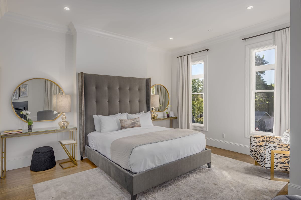A modern bedroom with a large bed, a vanity with a mirror, and a view of the outdoors.