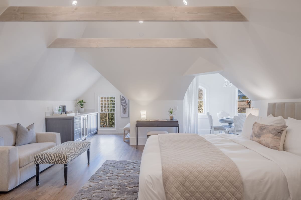 A spacious attic bedroom with a large bed, a sofa, and a desk area.