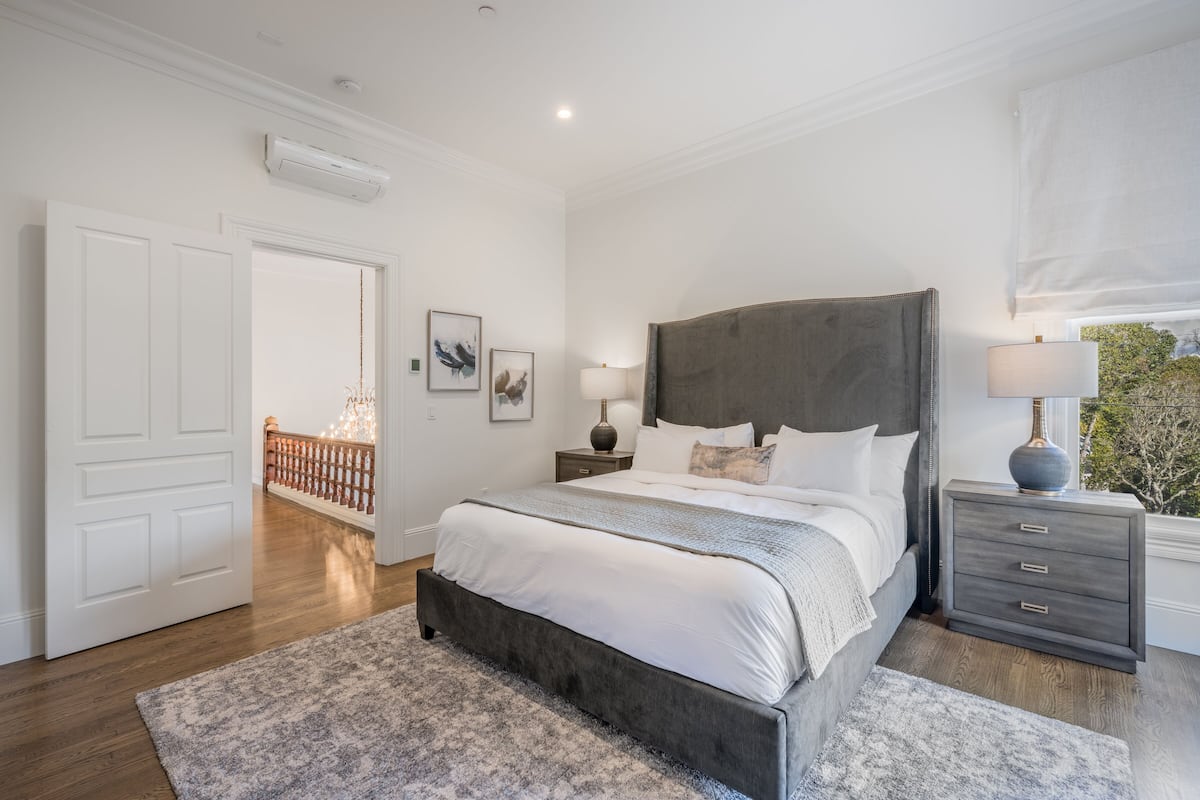 A bedroom with a large bed, bedside tables, a nightstand, a window with a view, and a door.