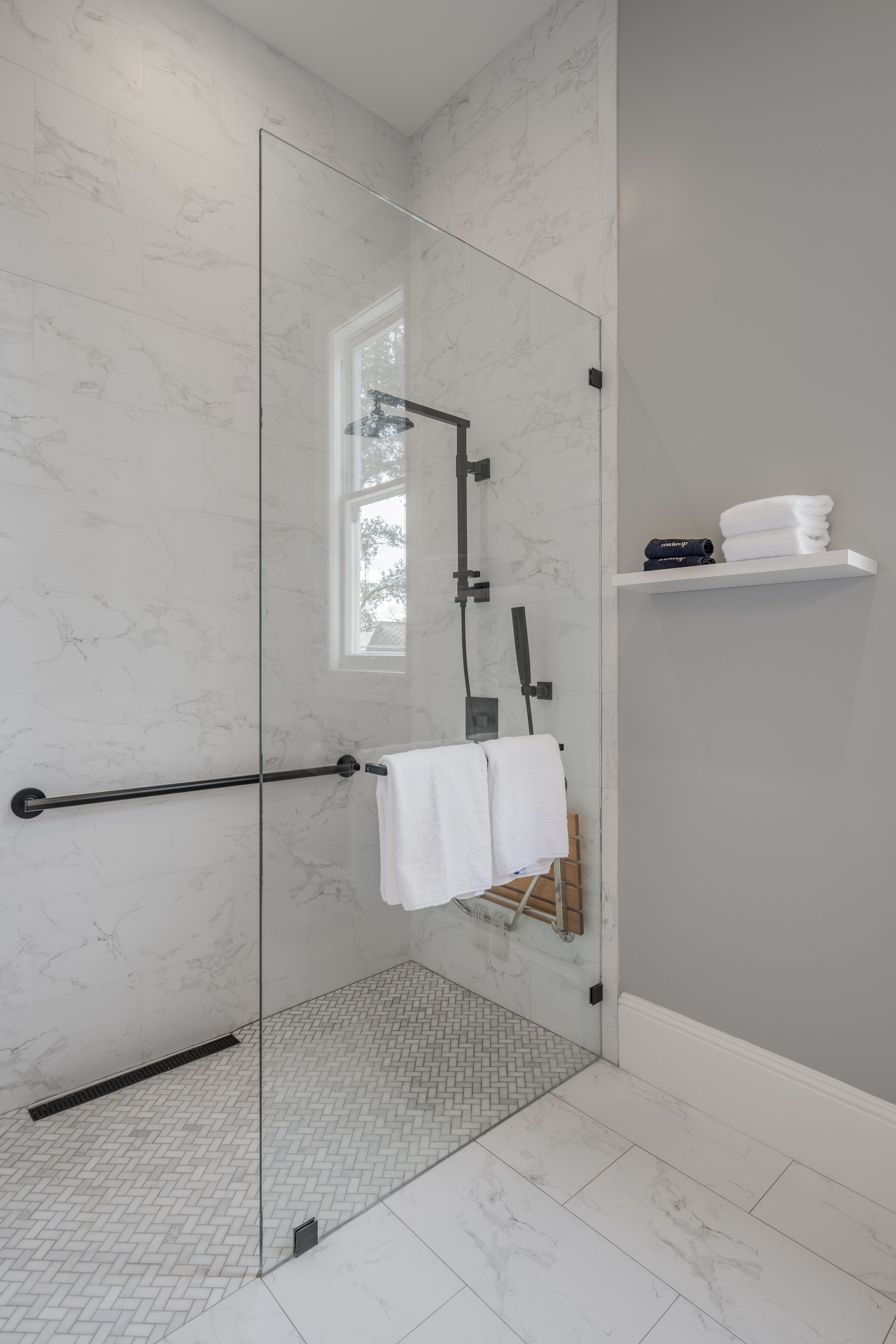 A modern bathroom with a glass shower enclosure, a black towel rack, and a white towel on the wall.