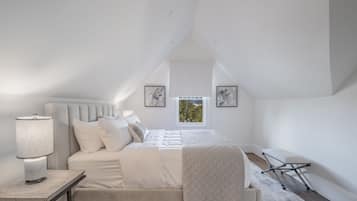 A bedroom with a bed, bedside table, lamp, and a window with a view.