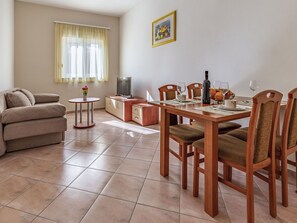 A living room with a sofa, a TV, a dining table with chairs, and a window with curtains.