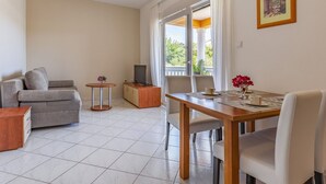 Un salon moderne comprenant un canapé, un téléviseur, une table à manger avec des chaises et un balcon avec des rideaux.