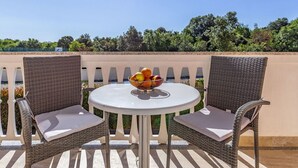 A round table with a bowl of fruit, two wicker chairs, and a view of trees and a fence.
