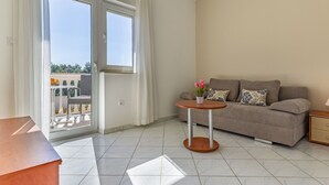 A modern living room with a grey sofa, a small round table, and a balcony with a view of the city.