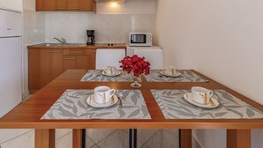Une cuisine compacte avec des meubles en bois, un four à micro-ondes et une machine à café. On y trouve une table à manger avec deux tasses et un vase rempli de fleurs rouges.