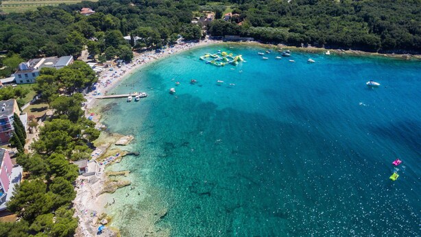 Vue aérienne d’une zone côtière avec des eaux turquoise limpides, une plage de sable et un petit quai.