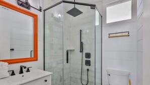 A modern bathroom with a glass-enclosed shower, a white sink with black faucets, and a white toilet. - Ocean View Studio#204-Newly Renovated! (New Smyrna Beach)