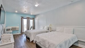 A hotel room with two beds, a desk with a chair, an air conditioning unit, and a window with curtains. - Ocean View Studio#204-Newly Renovated! (New Smyrna Beach)