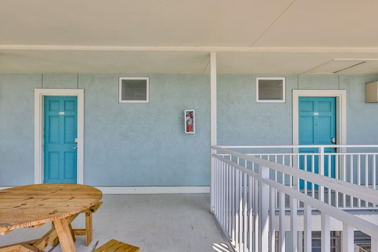 Um quarto com duas portas azul-turquesa, uma janela pequena e um corrimão branco.