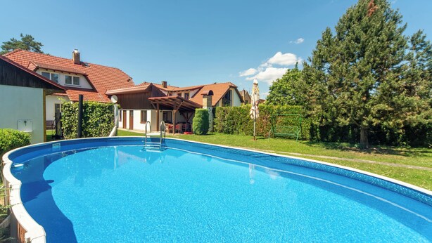 A swimming pool with a clear blue surface, surrounded by a well-maintained lawn and a wooden deck.