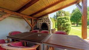 An outdoor patio with a stone oven, wicker furniture, and a view of a garden.