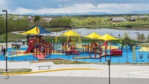 A playground with slides and climbing structures, surrounded by a body of water and greenery. - $0Fees; Near Park, Dining; Easy Access to Downtown (Northglenn)