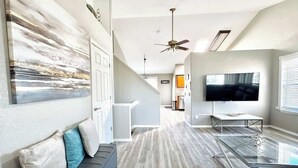 A modern living room with a glass coffee table, a grey sofa with cushions, a flat-screen TV, and a ceiling fan. - $0Fees; Near Park, Dining; Easy Access to Downtown (Northglenn)