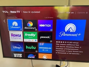 Ein TCL Roku Fernseher zeigt eine Auswahl an Streaming-Diensten, darunter Paramount+, Discovery+, HBO Max, Roku Channel und weitere.