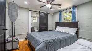 A bedroom with a bed, a ceiling fan, a window with curtains, and a door. - Tiny Home — Stylish Mt. Holly Retreat — 12 min to CLT & Whitewater Center (Mount Holly)