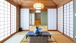 Une pièce de style japonais traditionnel, avec un sol recouvert de tatamis, des portes coulissantes et une table centrale agrémentée d’un vase décoratif.