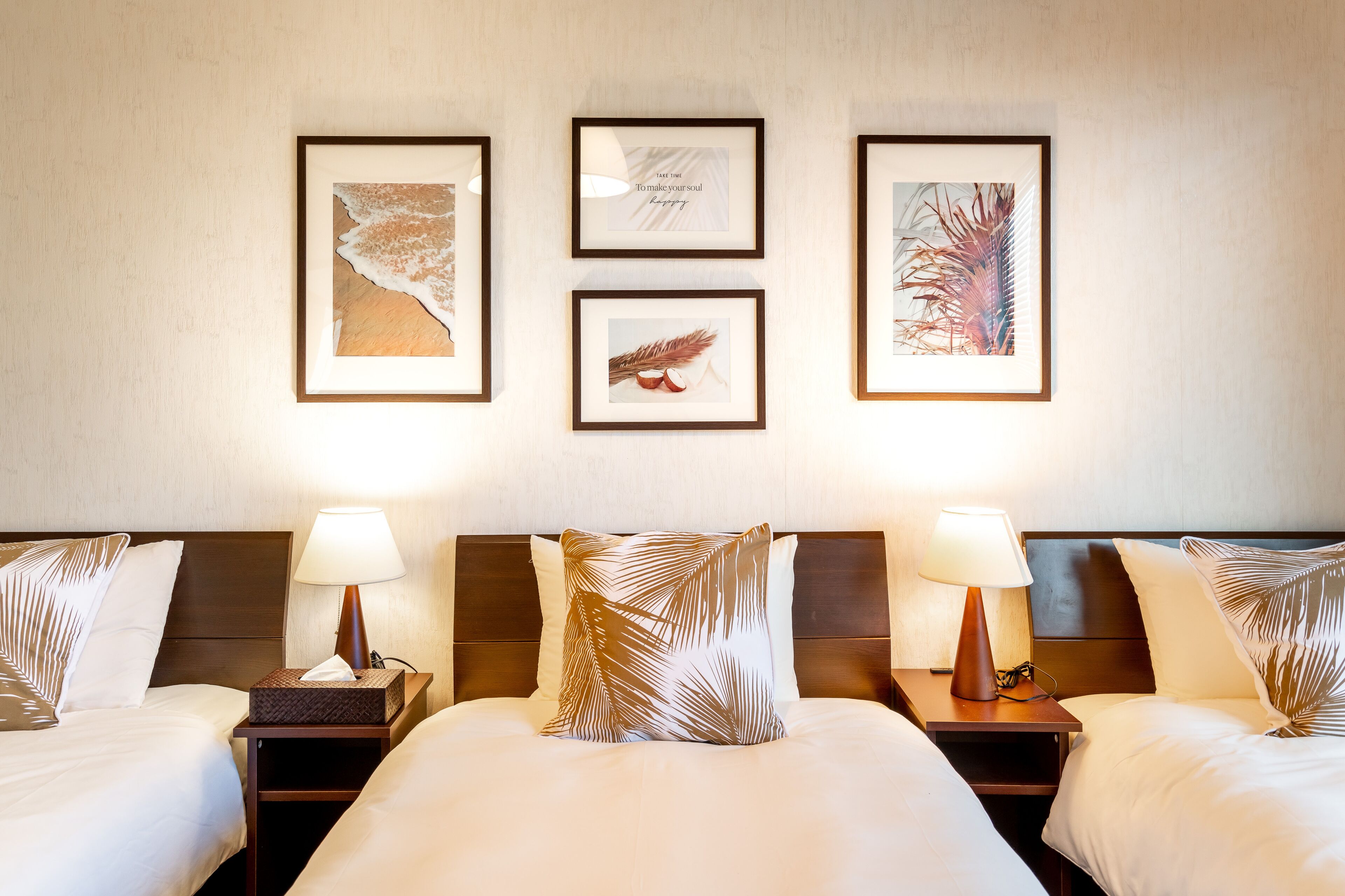 Quarto de hotel com duas camas, cada uma com mesa de cabeceira, abajur e um quadro emoldurado acima.