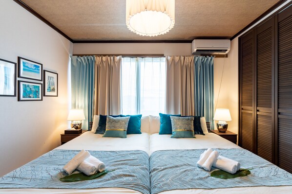 A double bed with a blue patterned bedspread, two pillows, and rolled towels on a leaf. - Ishigaki House (Ishigaki)