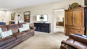 A living room with a brown leather sofa, a dark wooden cabinet, and a television displaying a logo. - Walk-In 2BR Royal Links Vacation Rental • Sleeps 6 (Branson)