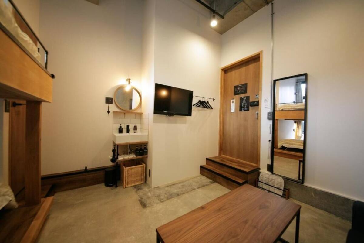 A compact room with a bunk bed, a small bathroom with a mirror, a TV, and a wooden table.