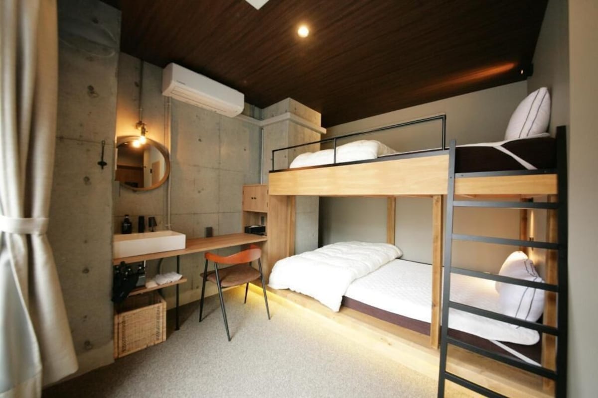 A compact bedroom with bunk beds, a desk, a chair, a mirror, and a small wardrobe.