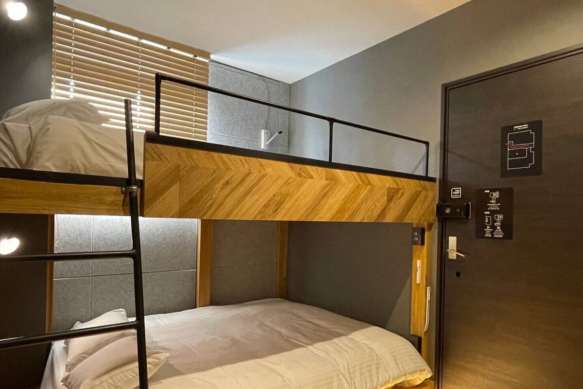 A bunk bed room with a wooden headboard, a door with emergency exit instructions, and a window with blinds.