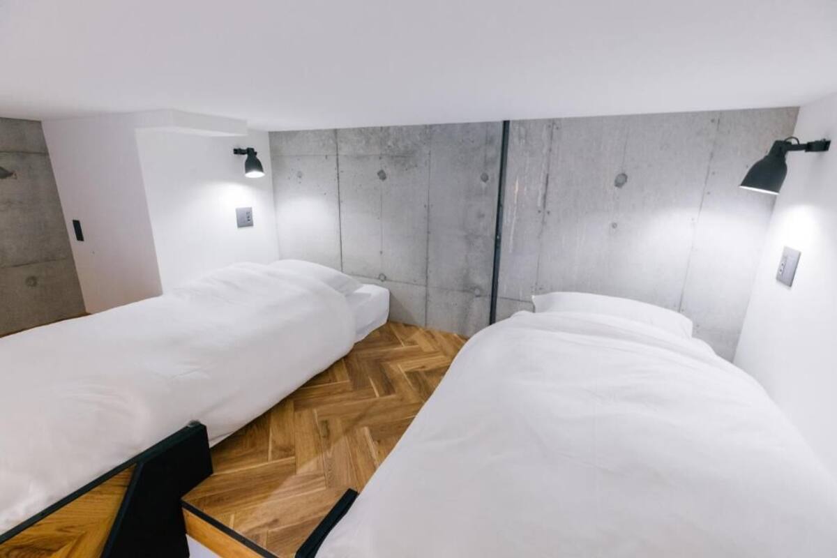 A room with two single beds, wooden flooring, and a concrete accent wall.