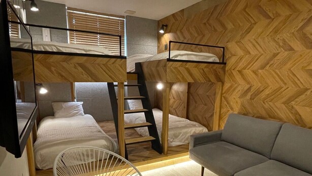 A compact room with bunk beds, a grey sofa, a white chair, and a small round table. - ZONK HOTEL HARUYOSHI-TERAMACHIDORI (Fukuoka)