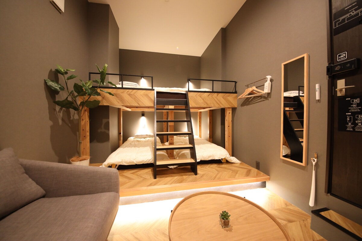 Une chambre avec un lit superposé, une échelle, une petite table avec une plante, un canapé et un miroir au mur.