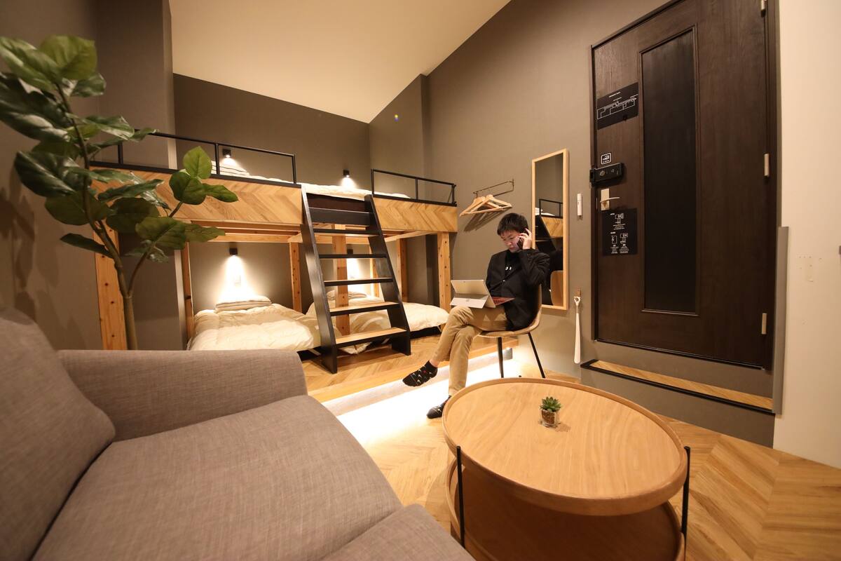 Una habitación moderna con literas, un sofá, una mesa redonda de madera y una planta en maceta.
