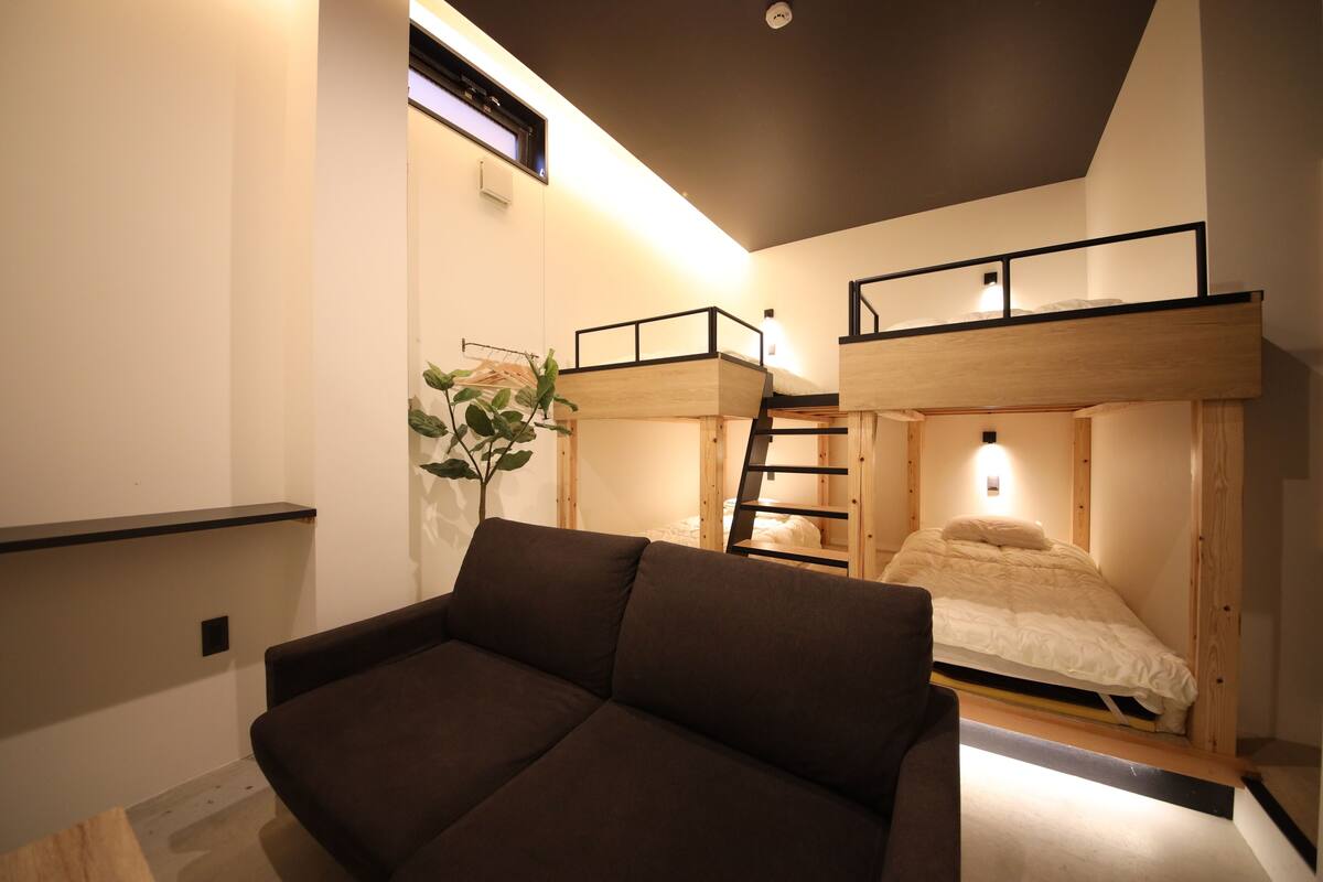 Una habitación compacta con una cama litera, un sofá y una pequeña planta.