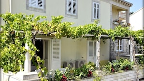 A building with a white facade, shutters, and a vine-covered pergola. - Immaculate 4-Bed House in Lumbarda (Lumbarda)