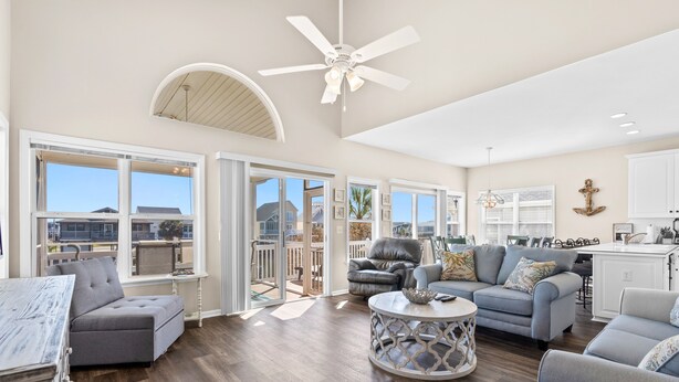A spacious living room with a grey sofa, a round coffee table, and a ceiling fan. - 4 Bedroom Canal Home! Great Location! (Ocean Isle Beach)