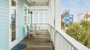Un pontile in legno con sedie e una porta, che si affaccia su un edificio blu e palme.